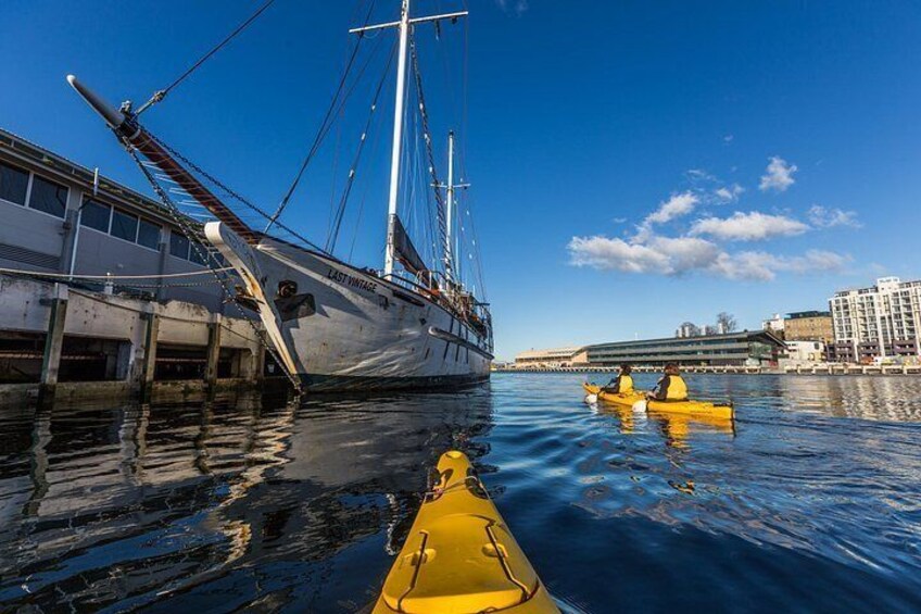 Ein großes Segelschiff liegt im Hafen vor Anker, im Hintergrund ist ein Gebäude zu sehen und im Wasser schwimmen zwei gelbe Kajaks. 5