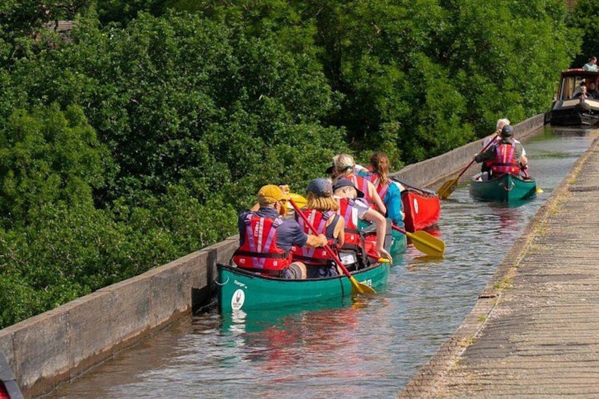 People in green canoes on a narrow waterway, surrounded by dense greenery. 3