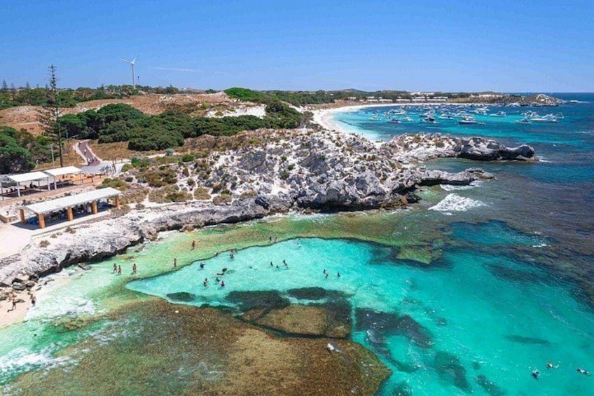 A coastal landscape with clear turquoise waters, rocky outcrops, and a beach area with people swimming. 2