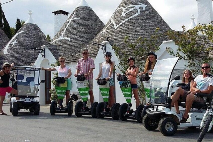 People riding Segway-like vehicles with 'TOURS' branding, parked in front of stone structures. 2