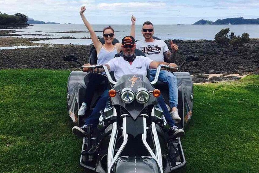 Tres personas en una motocicleta con un hermoso paisaje costero de fondo. 2
