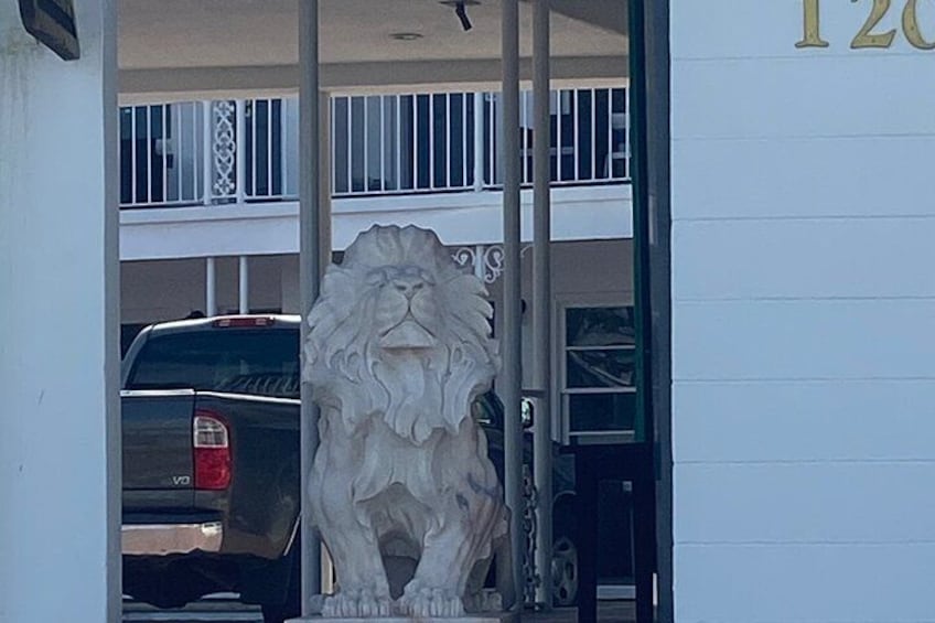 A lion statue at the entrance of a building with a balcony and a parked car. 2
