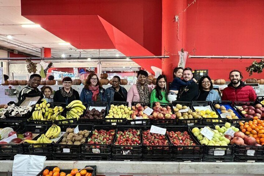 Un grupo de personas en un puesto de frutas y verduras con diversos productos como plátanos, manzanas y naranjas. 4