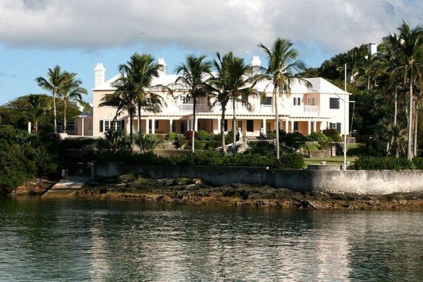 A coastal house with a white facade, palm trees, and a rocky shoreline. 2
