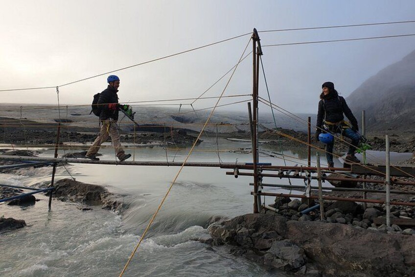 Two people crossing a suspension bridge over a river. 3