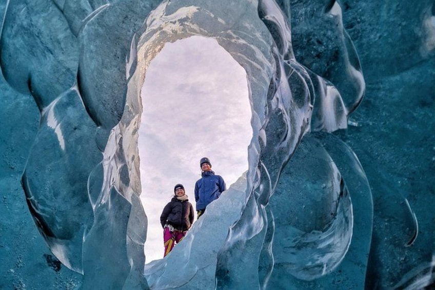 Dos personas de pie dentro de una cueva de hielo con una gran abertura. 3