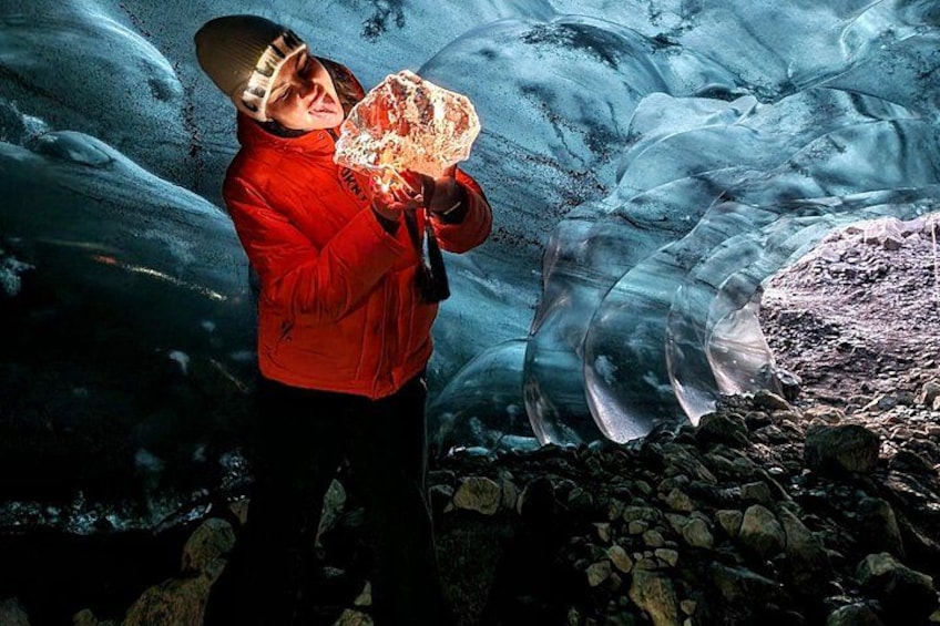 Una persona con una chaqueta roja sostiene un objeto transparente frente a un glaciar. 5
