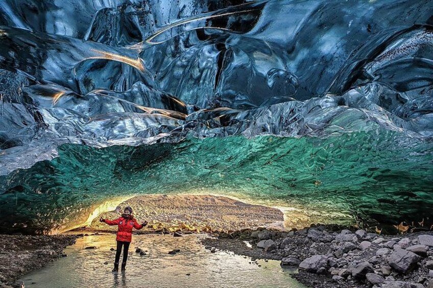 A person standing in a cave with ice formations and a river. 4