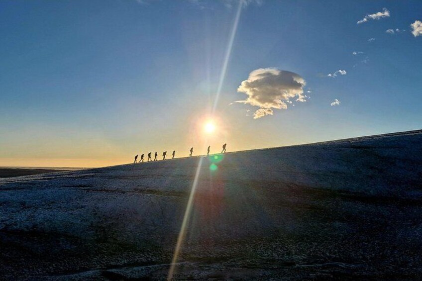 A group of people walking on a snow-covered slope during sunset. 2