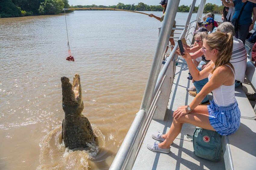 Een krokodil op een boot, mensen die kijken, en een rustige rivier. 3
