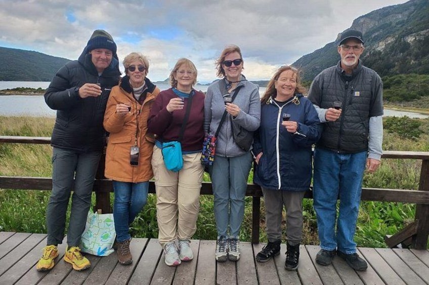 A group of people standing on a wooden deck by a lake with mountains in the background. 1