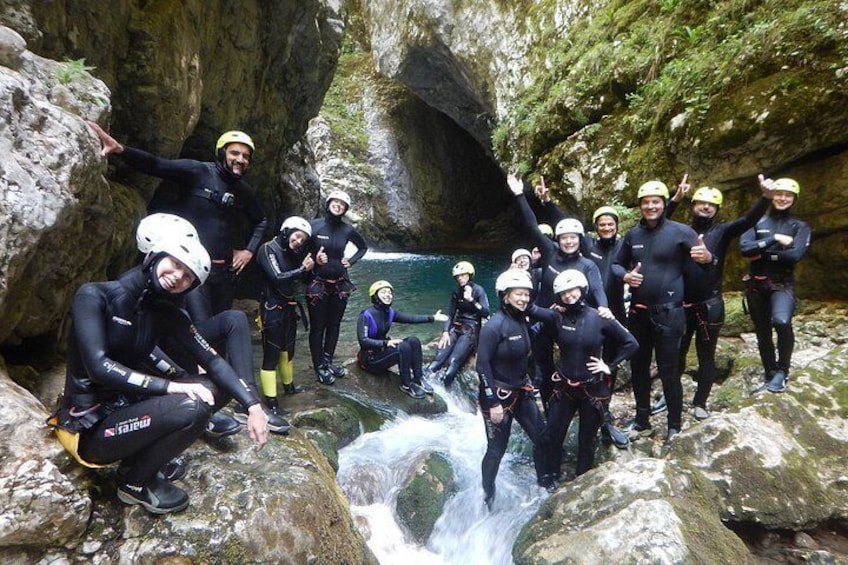 A group of people in wetsuits and helmets near a waterfall in a rocky canyon. 1