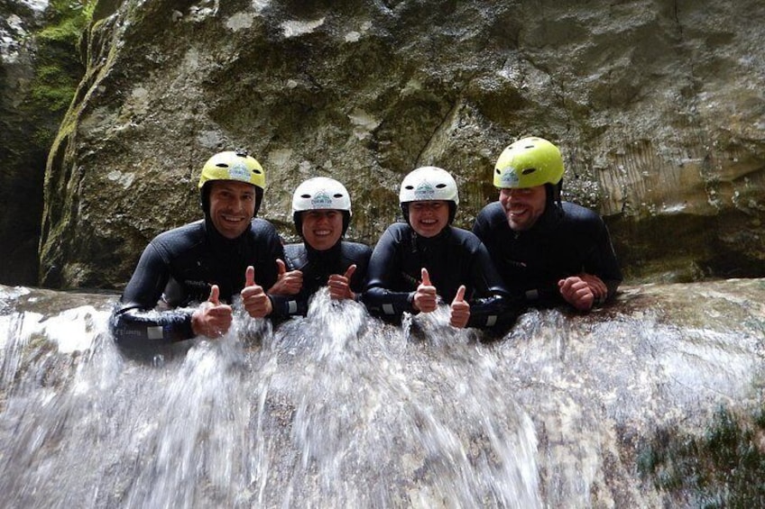 Four people in wetsuits and helmets sitting on a rock by a waterfall. 5