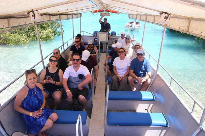 A boat with people seated on blue cushioned benches, a canopy overhead, and calm water in the background. 5