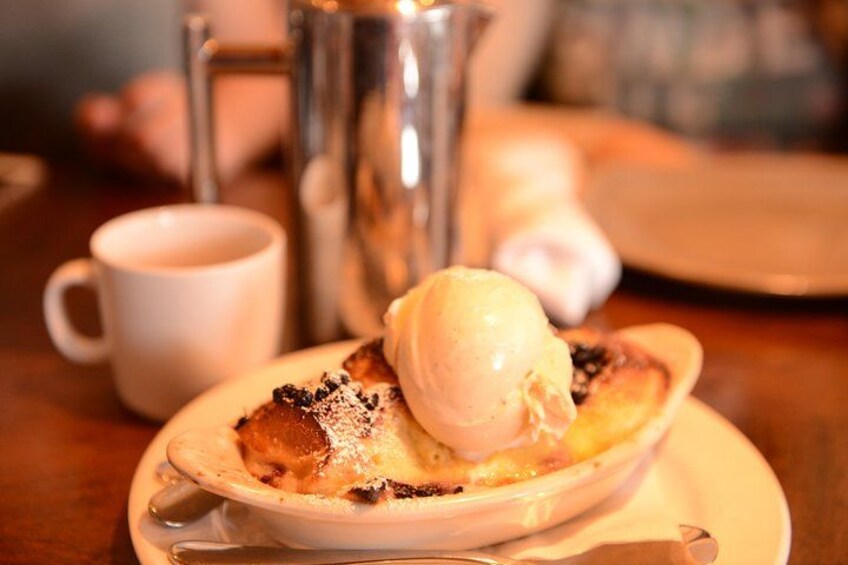 Un plato con postre, una bola de helado, un trozo de pastel, una taza blanca y una jarra de plata sobre una mesa de madera. 1