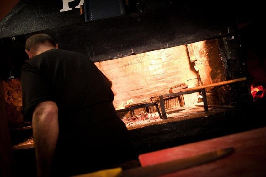 Una persona trabajando en un horno de ladrillo, posiblemente un horno para pizza, con una herramienta de madera y una barra de metal. 3