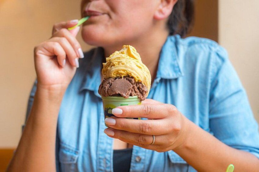 Una persona sosteniendo una taza de helado con dos porciones, una amarilla y otra marrón. 2