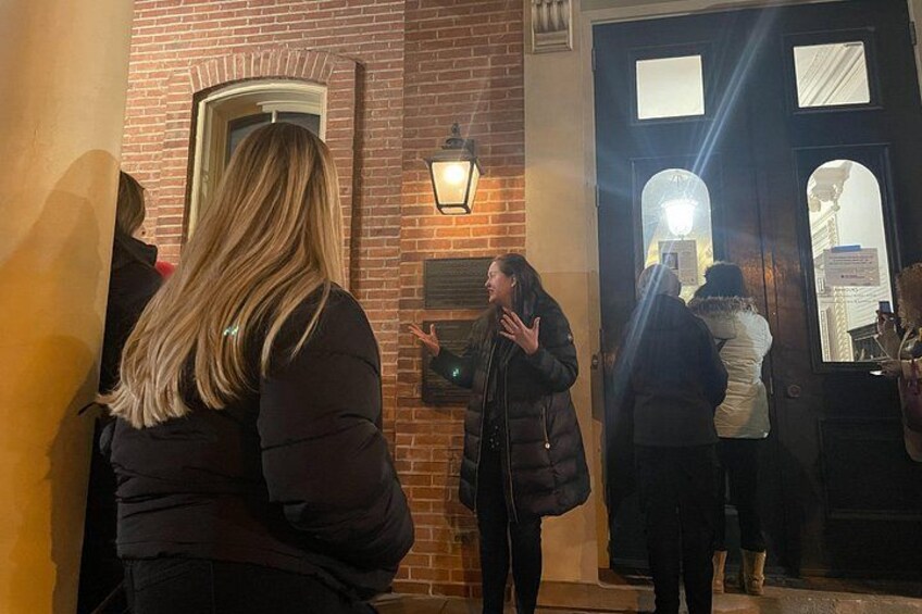 Un edificio de ladrillo con una puerta y una ventana, una persona de pie frente a él, y otra alejándose caminando. 3