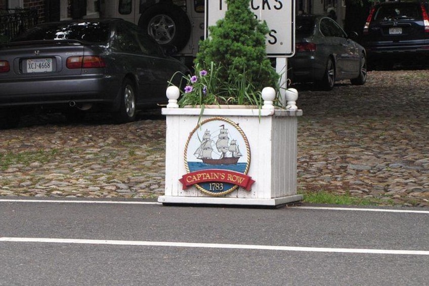 Ein Straßenschild mit weißem Grund und einem roten Banner, das 'Captain's Row 1783' zeigt. 5