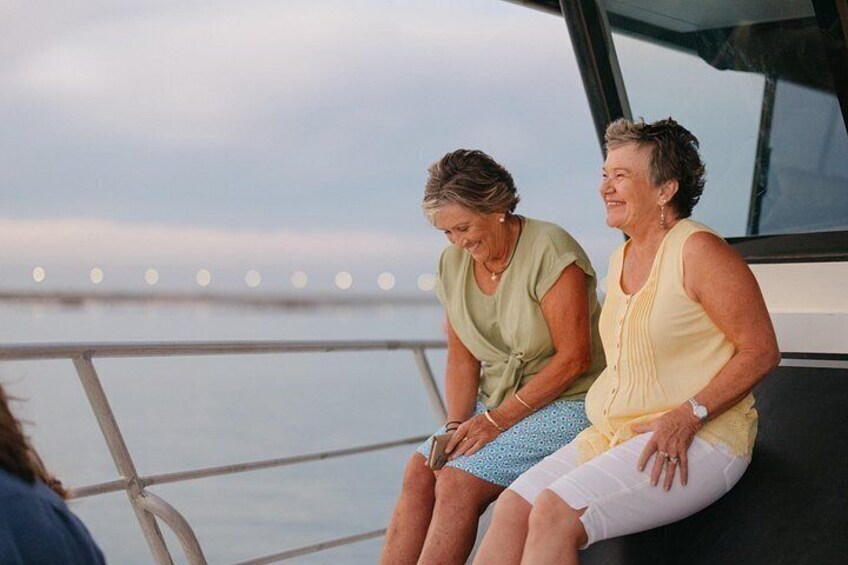 Two people sitting on a boat with a railing and water in the background. 3