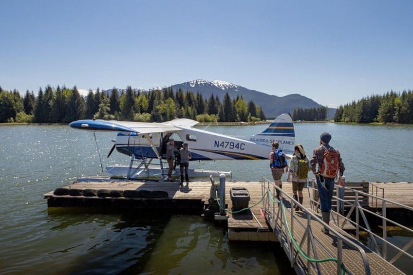 A seaplane on a dock with people boarding, surrounded by a lake and mountains. 1