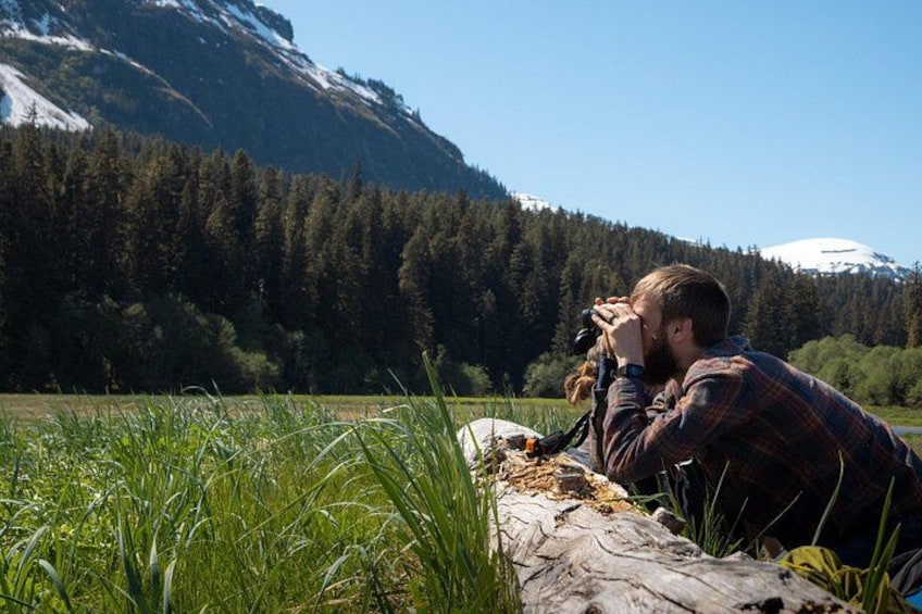 Une personne prend une photo dans un champ herbeux, avec des montagnes en arrière-plan. 4