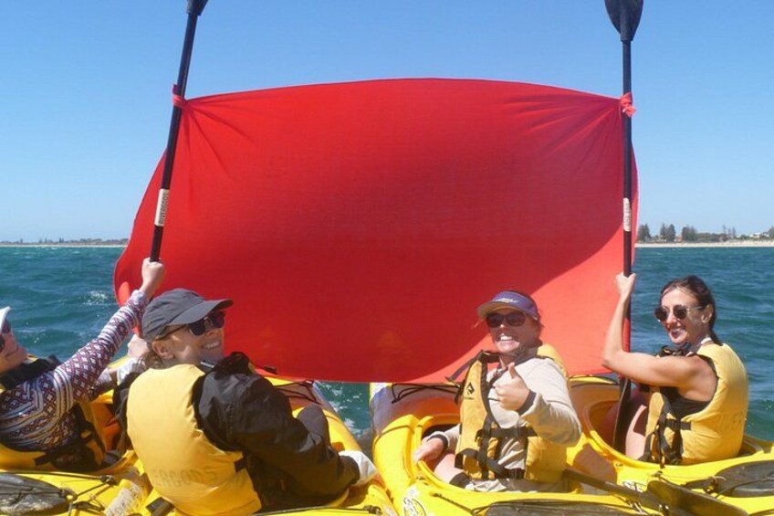 A group of people in a yellow kayak on a body of water, holding a red sail. 2