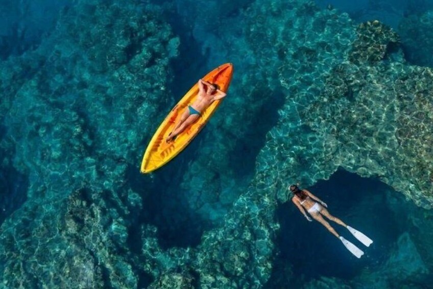 Two people floating on a clear blue sea, one on a yellow surfboard and the other on a paddleboard. 1