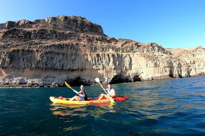 Dos personas hacen kayak en un mar tranquilo con acantilados rocosos al fondo. 5