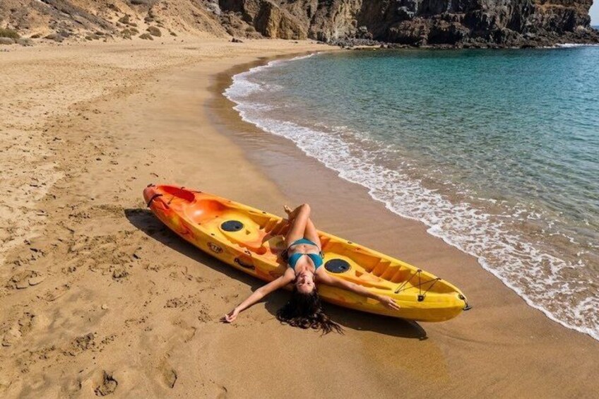A person lying on a sandy beach with a yellow kayak nearby. 3