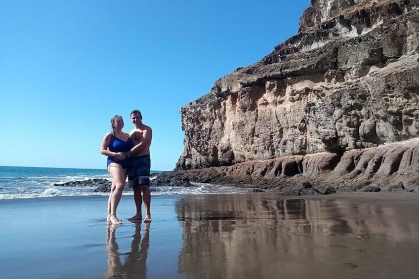 A couple standing on a beach with a rocky cliff in the background. 4
