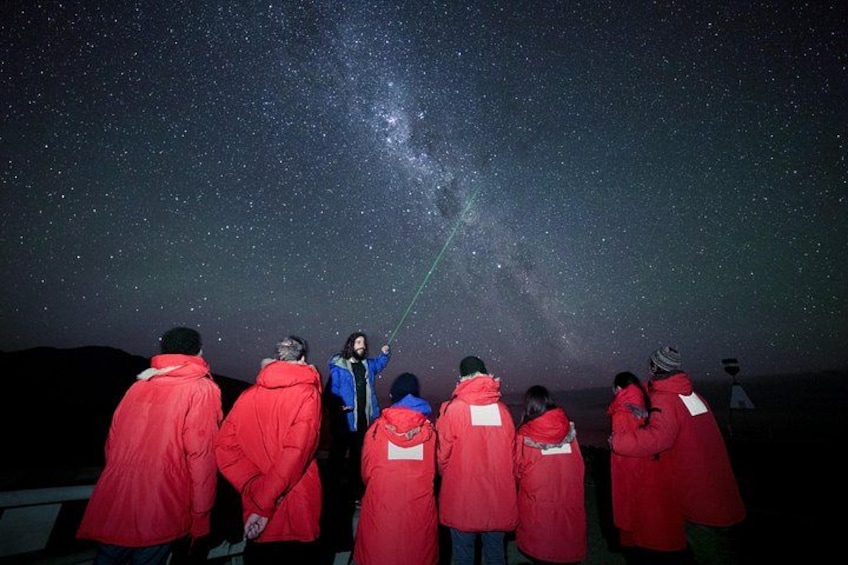 Un grupo de personas con chaquetas rojas observando el cielo nocturno, con la Vía Láctea visible. 2