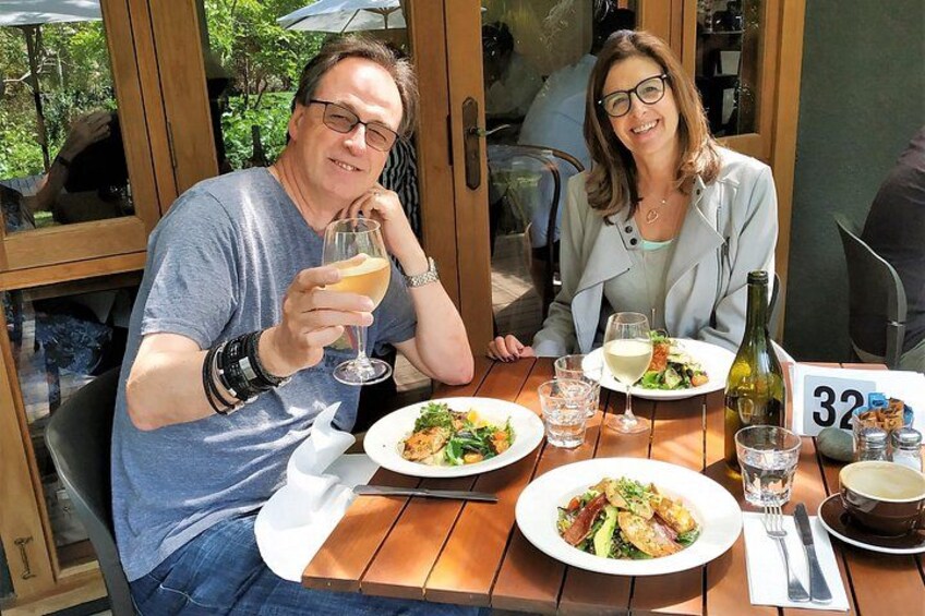 Dos personas cenando en una mesa al aire libre, con platos de comida, copas de vino y una botella. 5