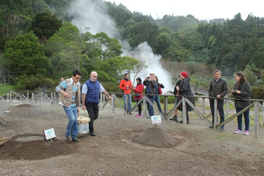 A group of people observing a steam vent, with a forested hillside in the background. 3