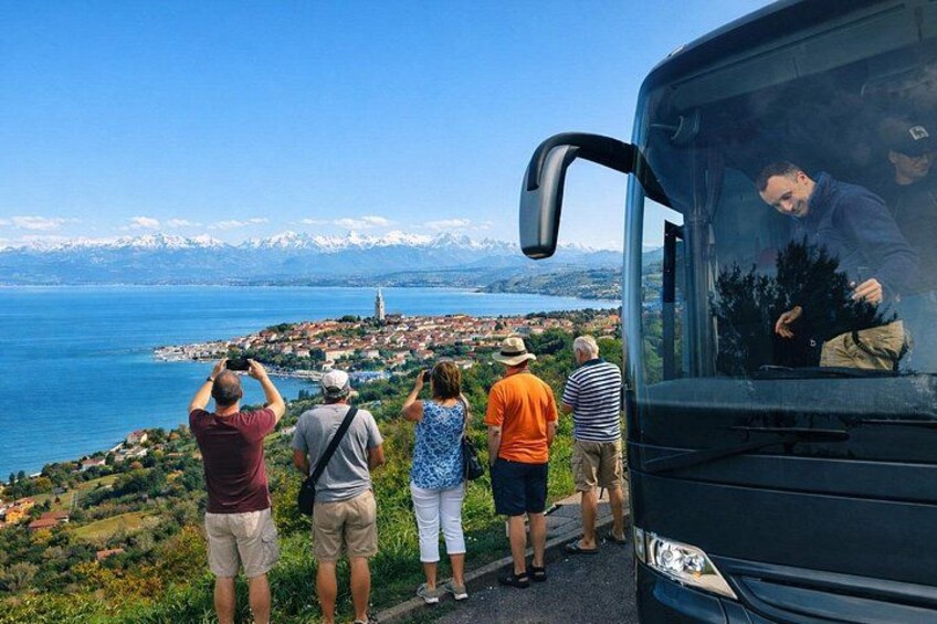 En gruppe mennesker tager et billede, en bus og et kystlandskab med bjerge i baggrunden. 2
