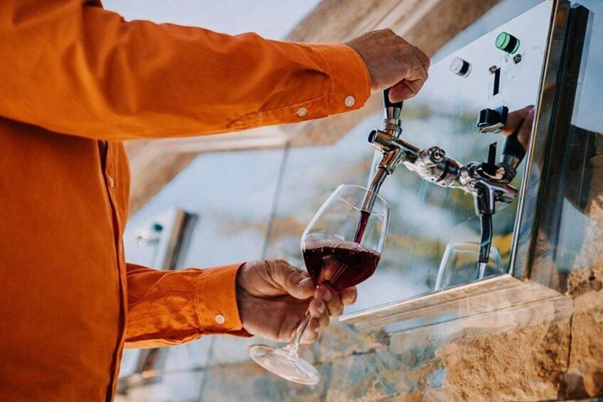 En person i orange trøje hælder vin fra en hane i et glas. 5