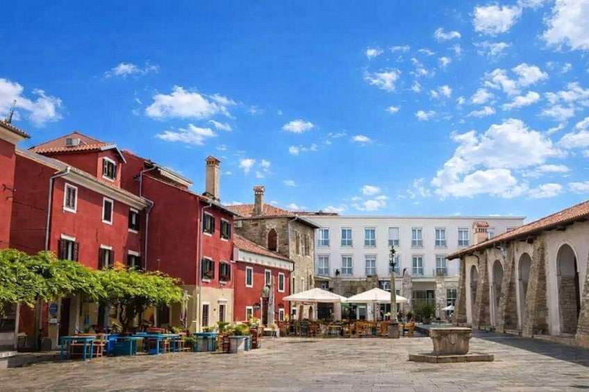 A square with red and white buildings, a fountain, and outdoor seating. 4