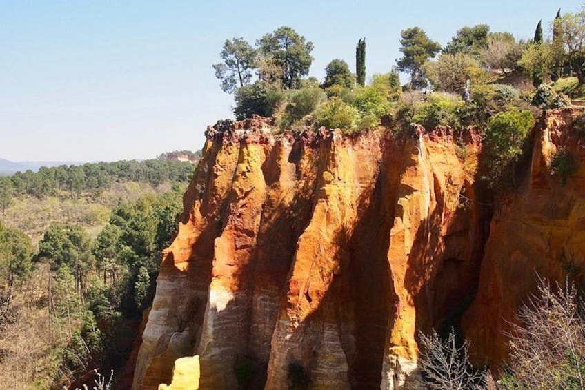 A large, reddish-brown cliff with vertical striations, surrounded by a forested landscape. 2