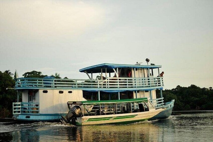 A large houseboat with multiple decks and a blue roof, floating on calm water. 2