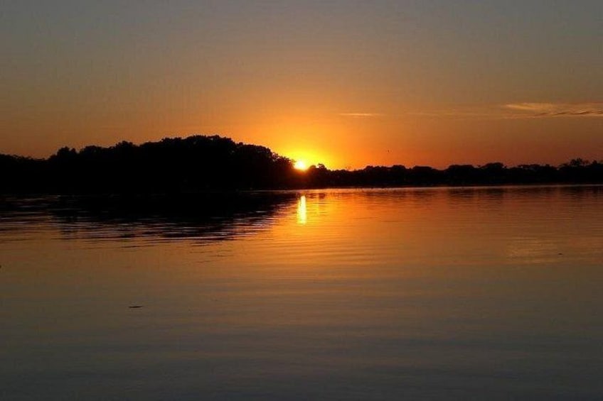 A sunset over a calm body of water with a silhouette of trees on the horizon. 4