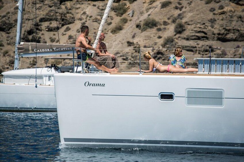 A yacht named 'Orama' with people on deck, a rocky shoreline, and another yacht in the background. 4