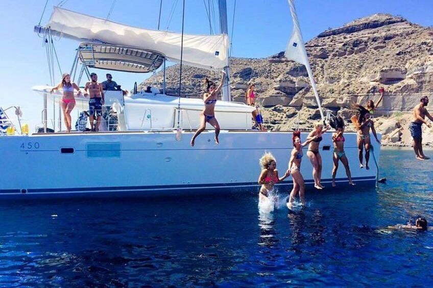 People on a boat, some jumping into the water, with rocky hills in the background. 2