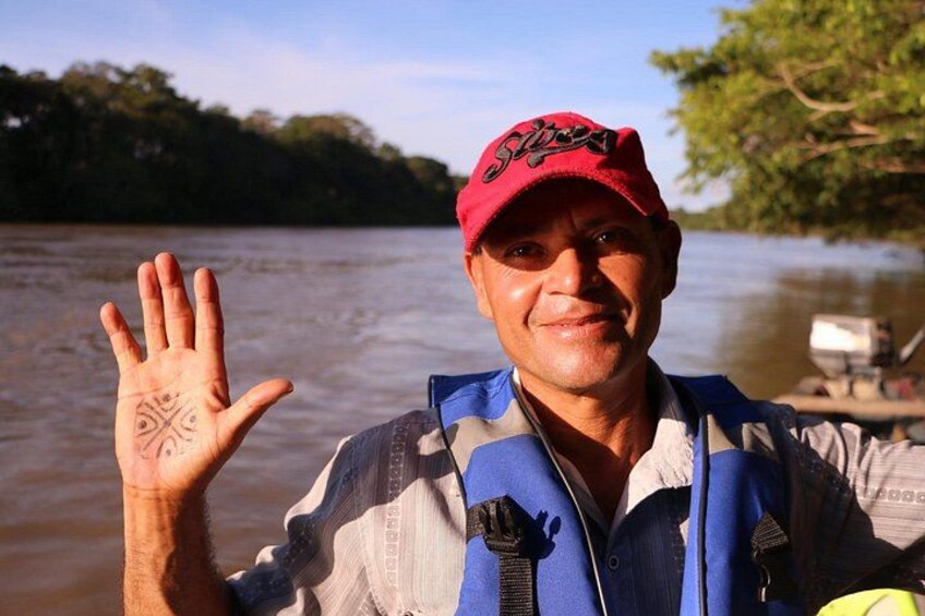 A person wearing a red cap and a blue life jacket, standing on a boat with a river in the background. 2