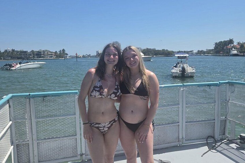 Two people on a dock with a body of water, boats, and buildings in the background. 2