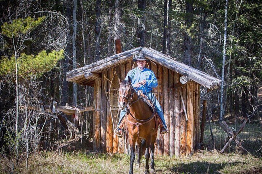 Eine Person zu Pferd vor einem rustikalen Holthaus. 2