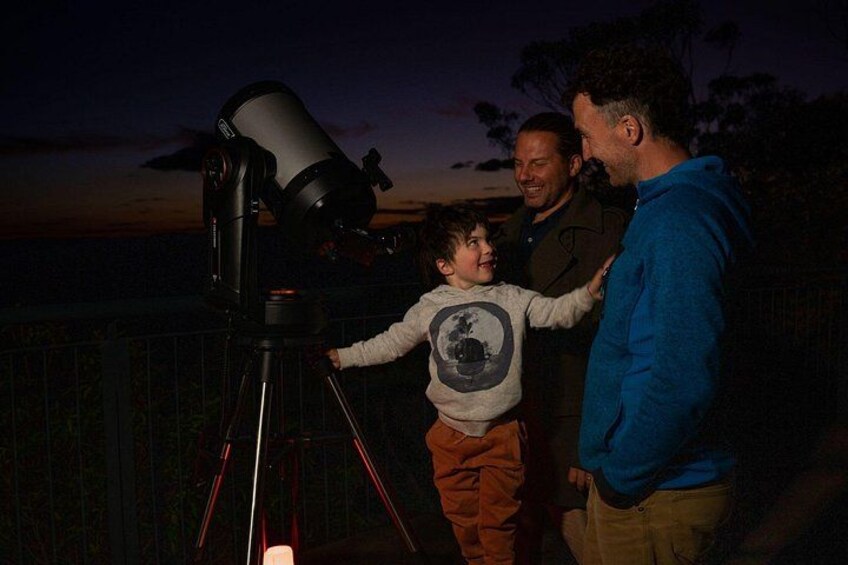 A telescope on a tripod, a person in a blue hoodie, and two others standing nearby. 3