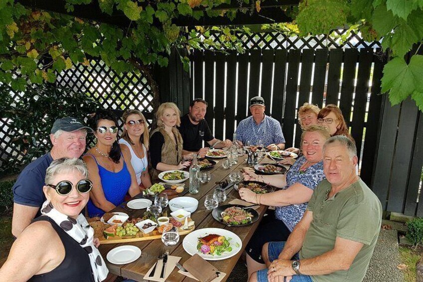 A group of people dining outdoors at a wooden table with various dishes and drinks. 4