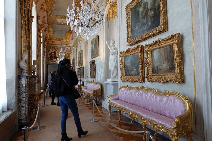 An opulent room with a pink sofa, gold-framed paintings, and a chandelier. 2