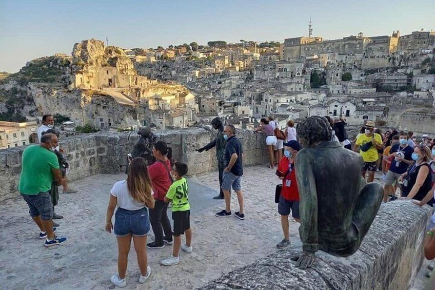 A group of people on a stone platform overlooking a historic cityscape with ruins and buildings. 1