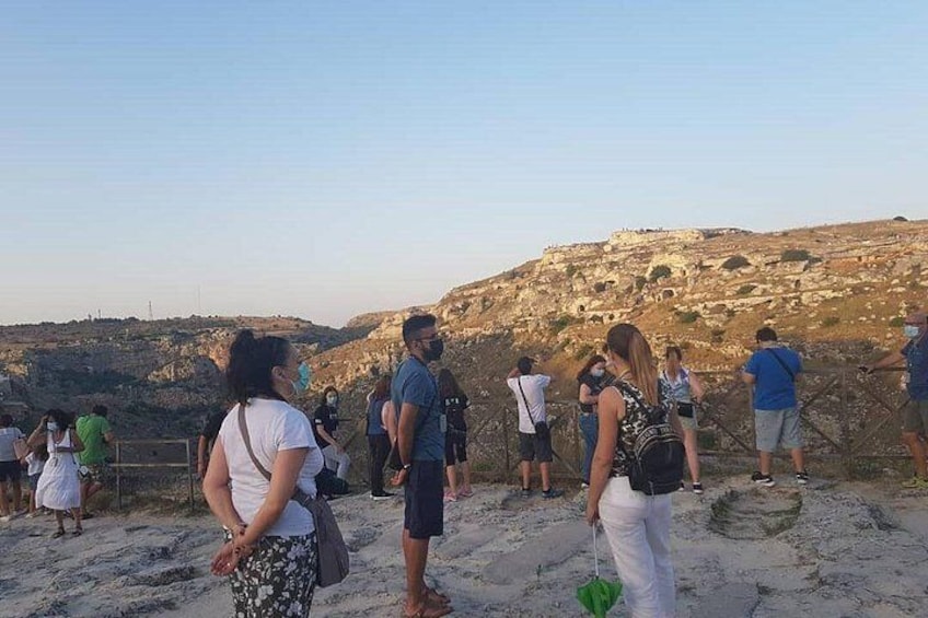 A group of people standing on a sandy beach, overlooking a rocky hill with ruins. 2